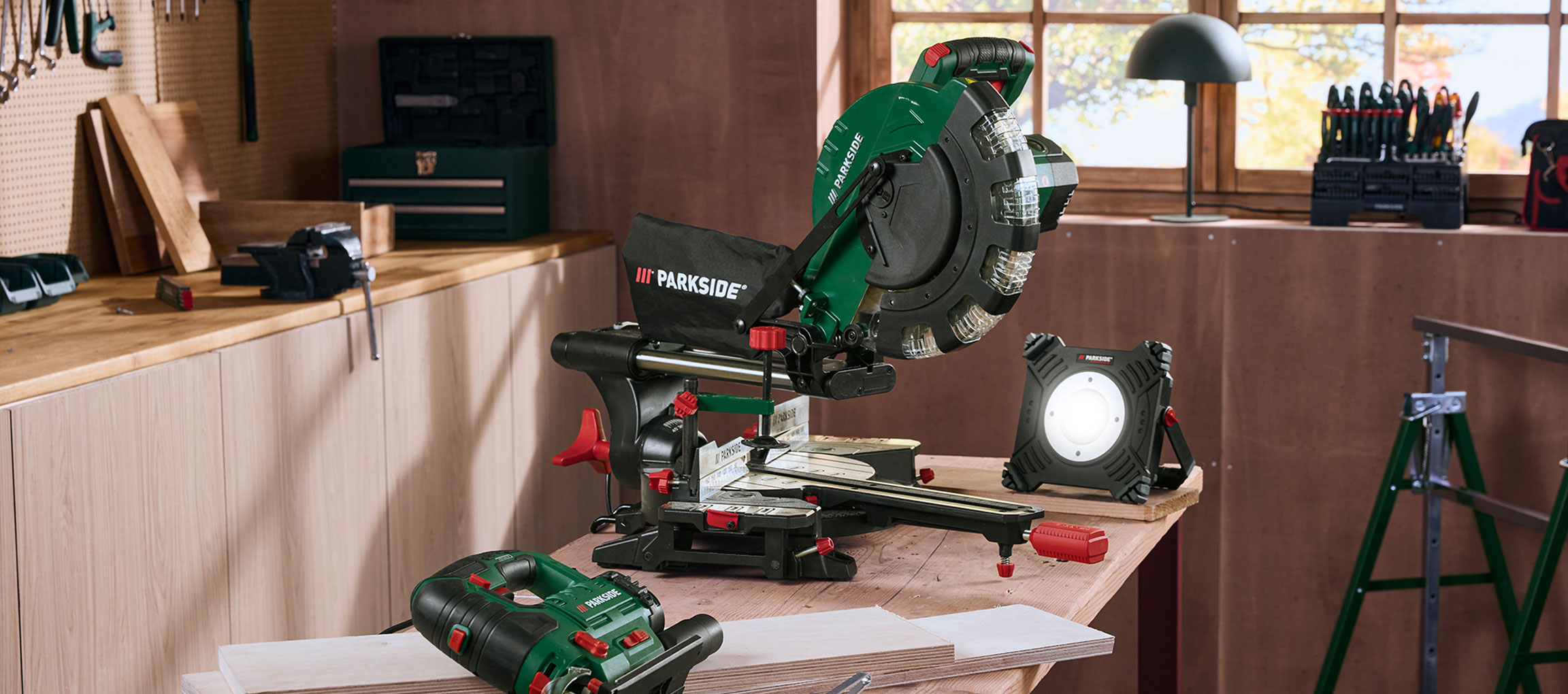 Workshop with a miter saw, workshop light, and other tools on a wooden table.