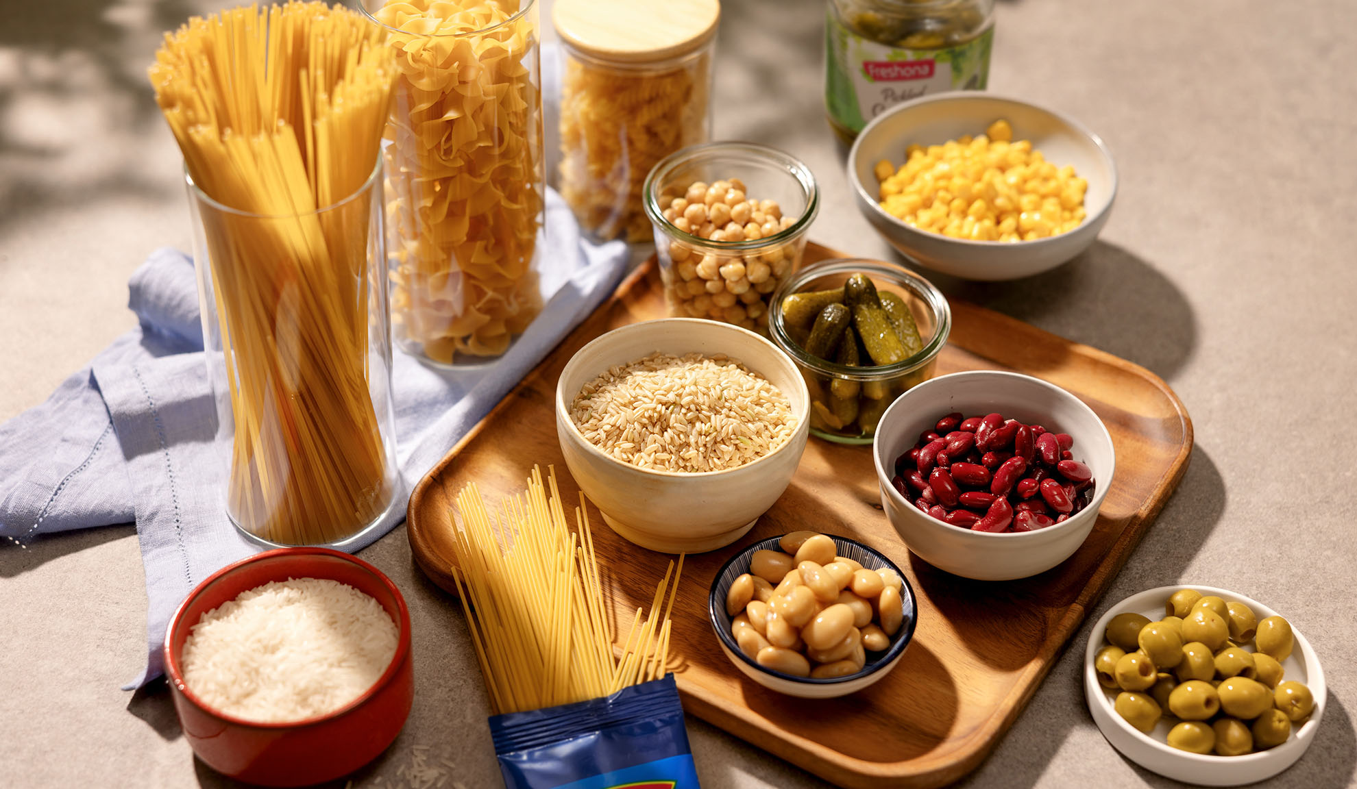 Assortment of dry pasta, rice, chickpeas, beans, corn, pickles, and olives.