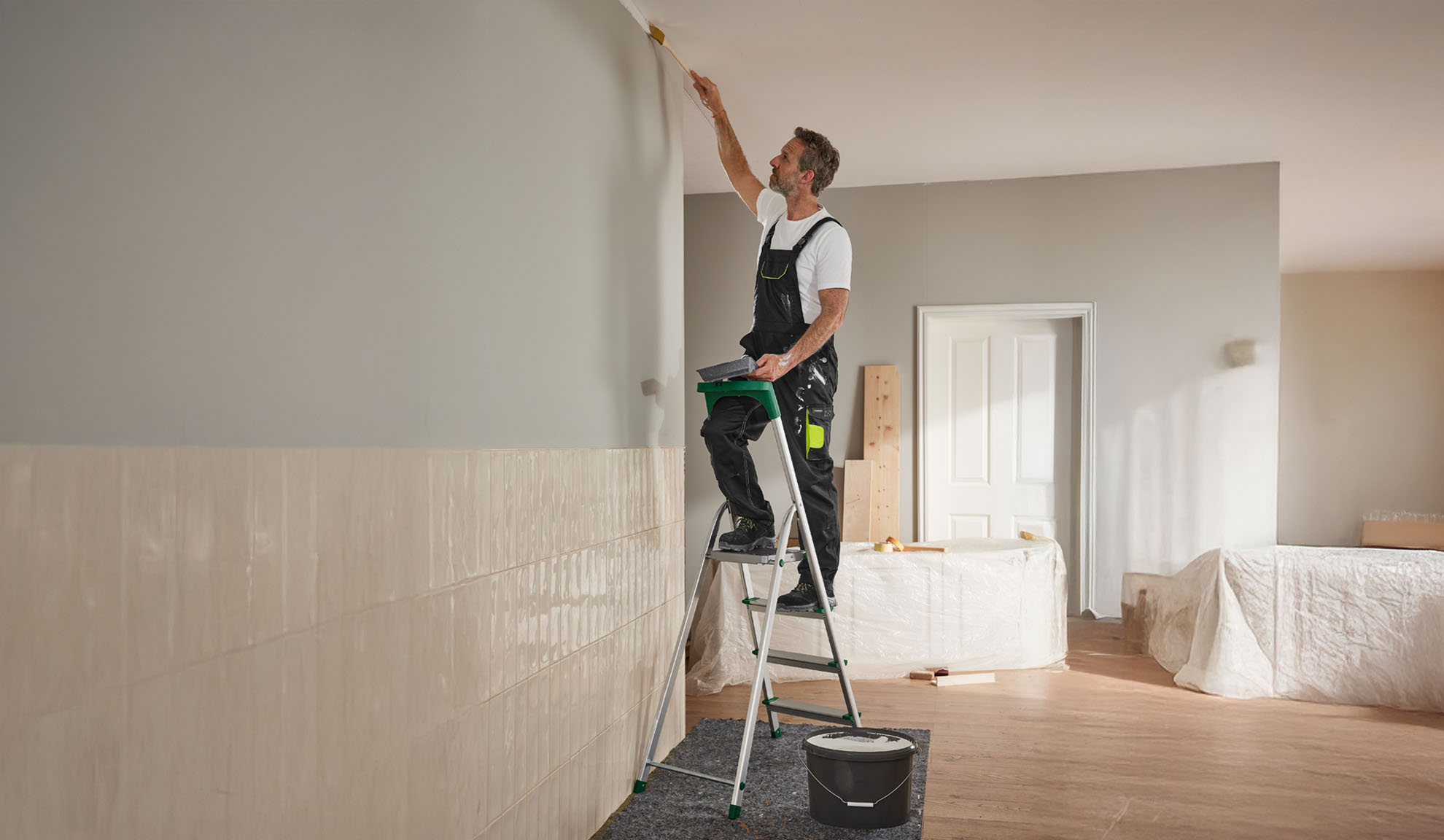 A man paints a wall using a stepladder and a paintbrush.