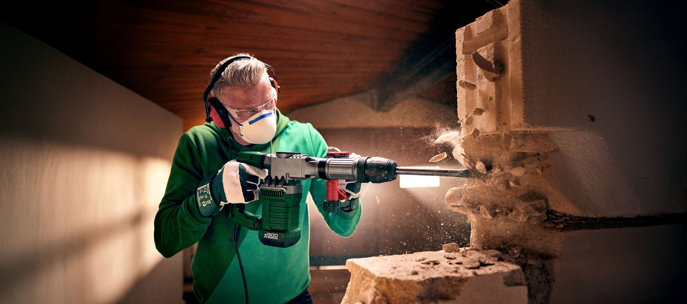 A man uses a Bosch X1300 demolition hammer to break a concrete block wall.
