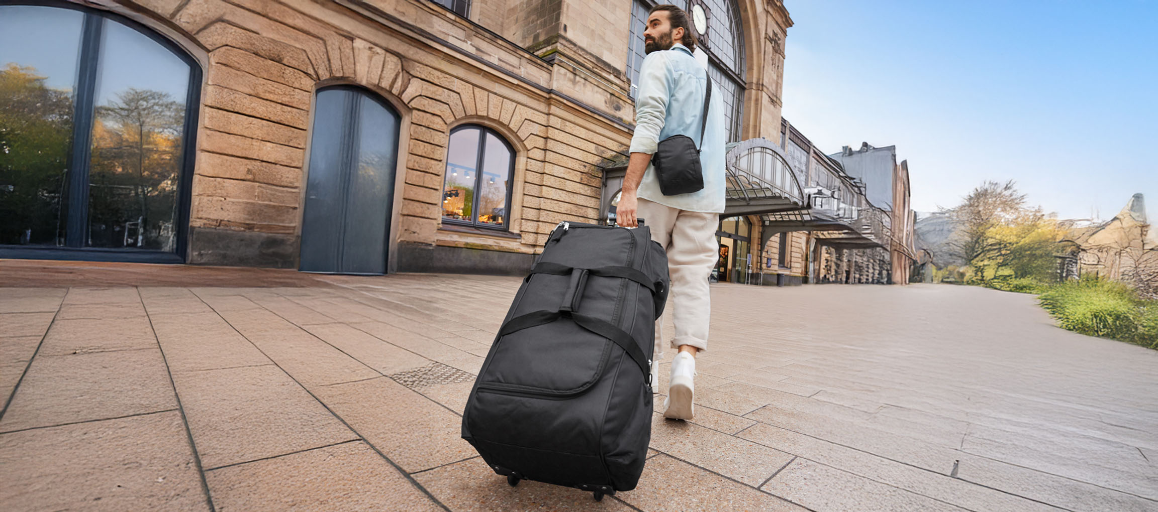 A man pulls a wheeled duffel bag away from a train station.