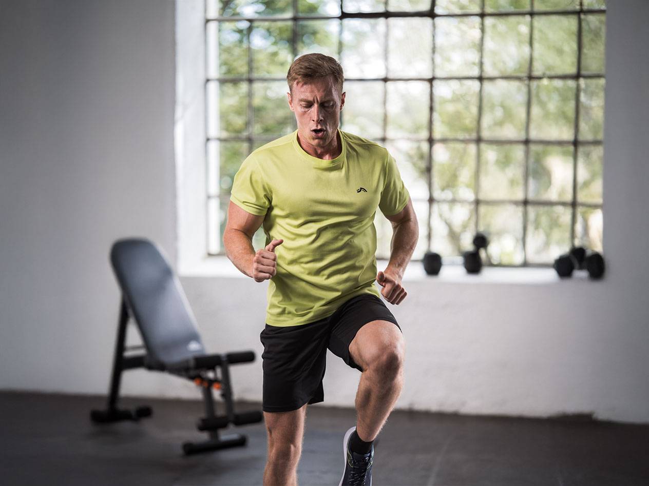 Man in a yellow t-shirt and black shorts running in a gym.