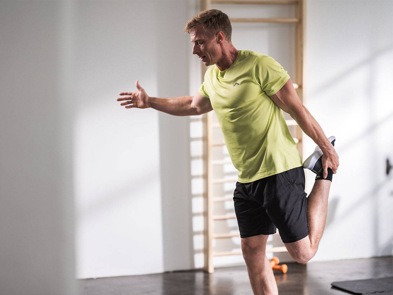 Man stretching in black shorts and a lime green t-shirt in a gym.