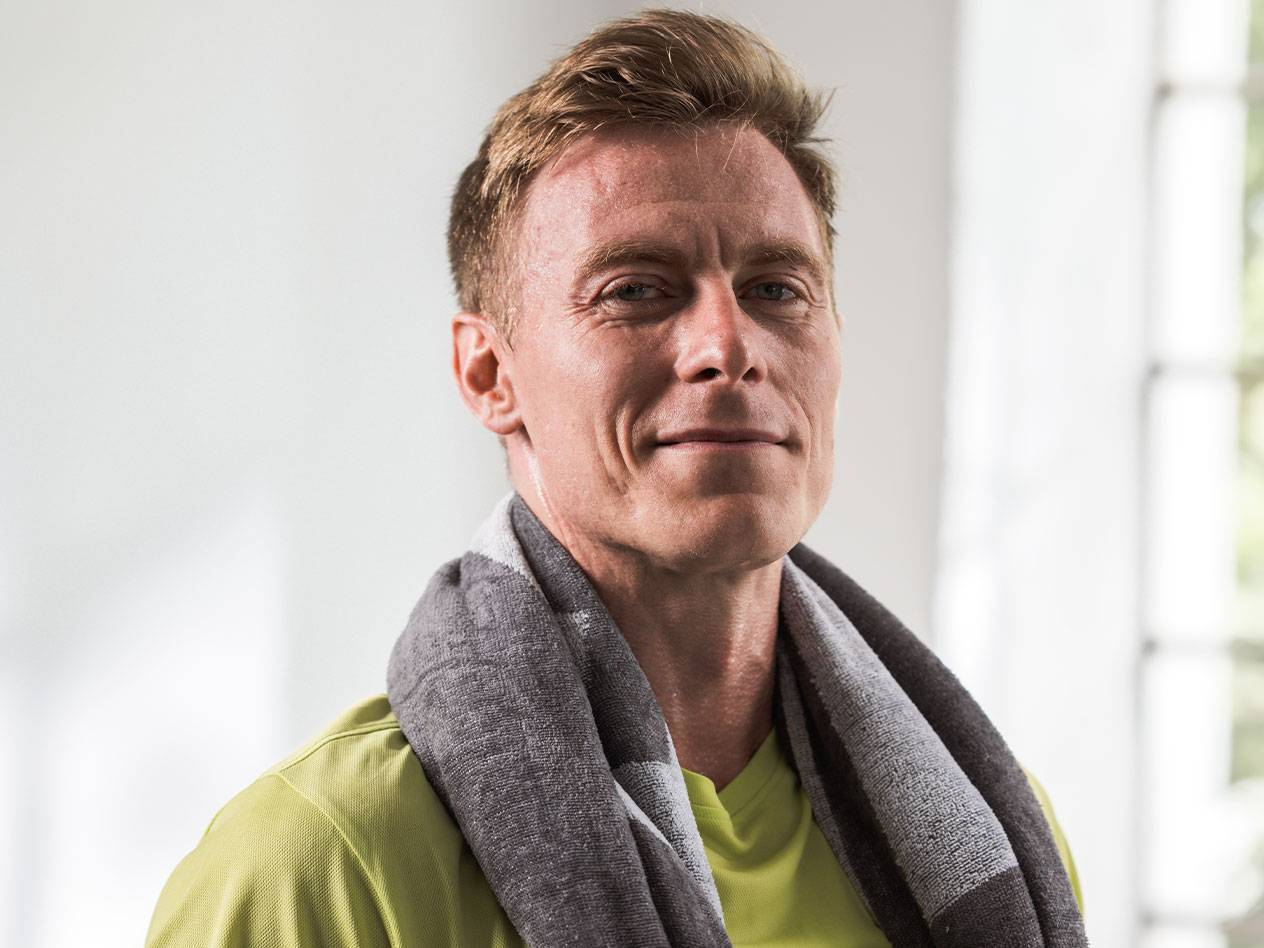 A blond man with a towel around his neck looks at the camera.