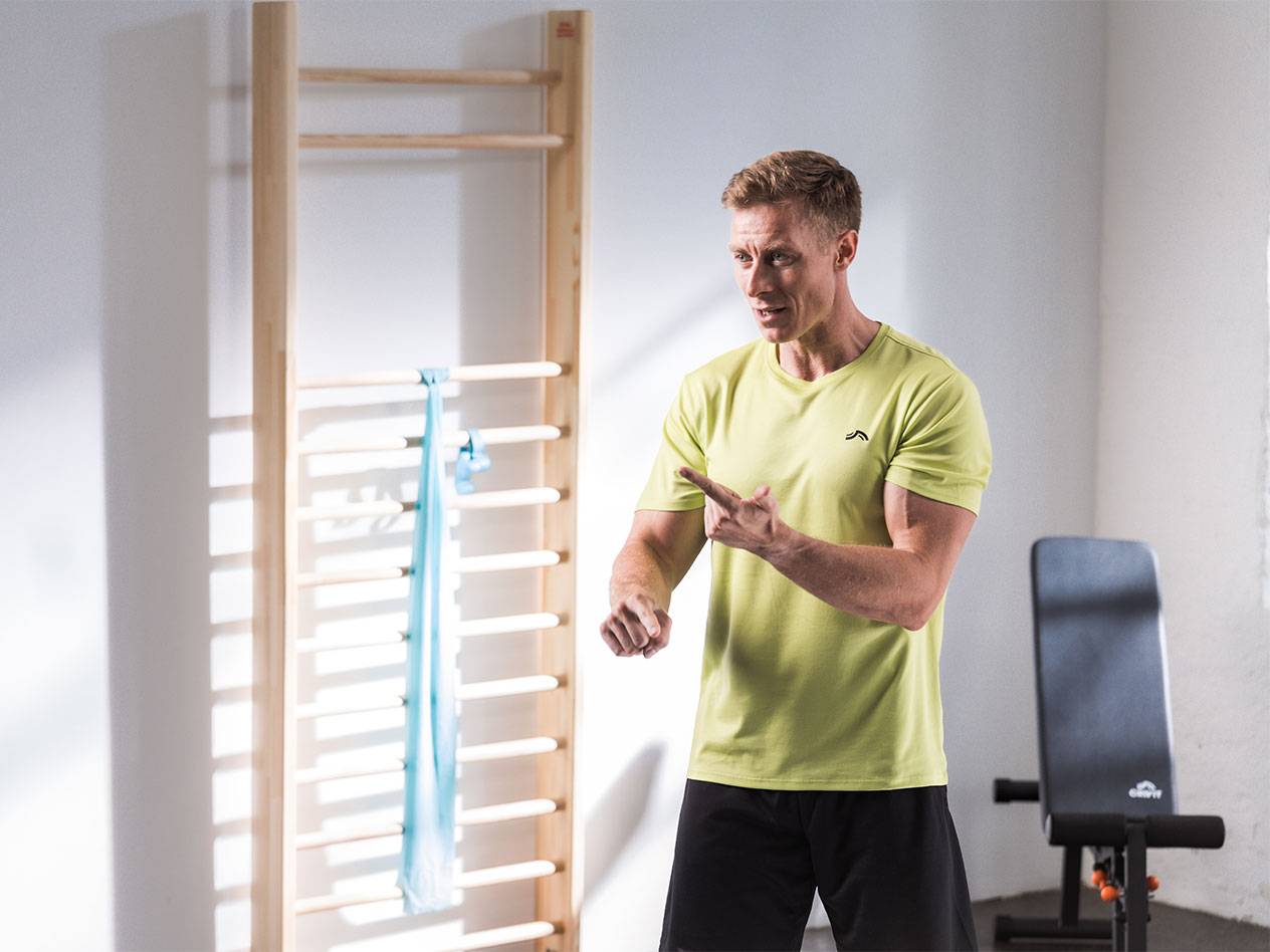 A man in athletic wear standing in front of a stall bar with a resistance band.