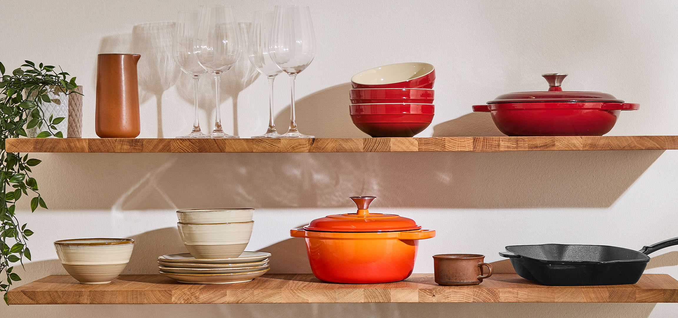 Kitchen shelves with red and orange pots, beige bowls, and glasses.