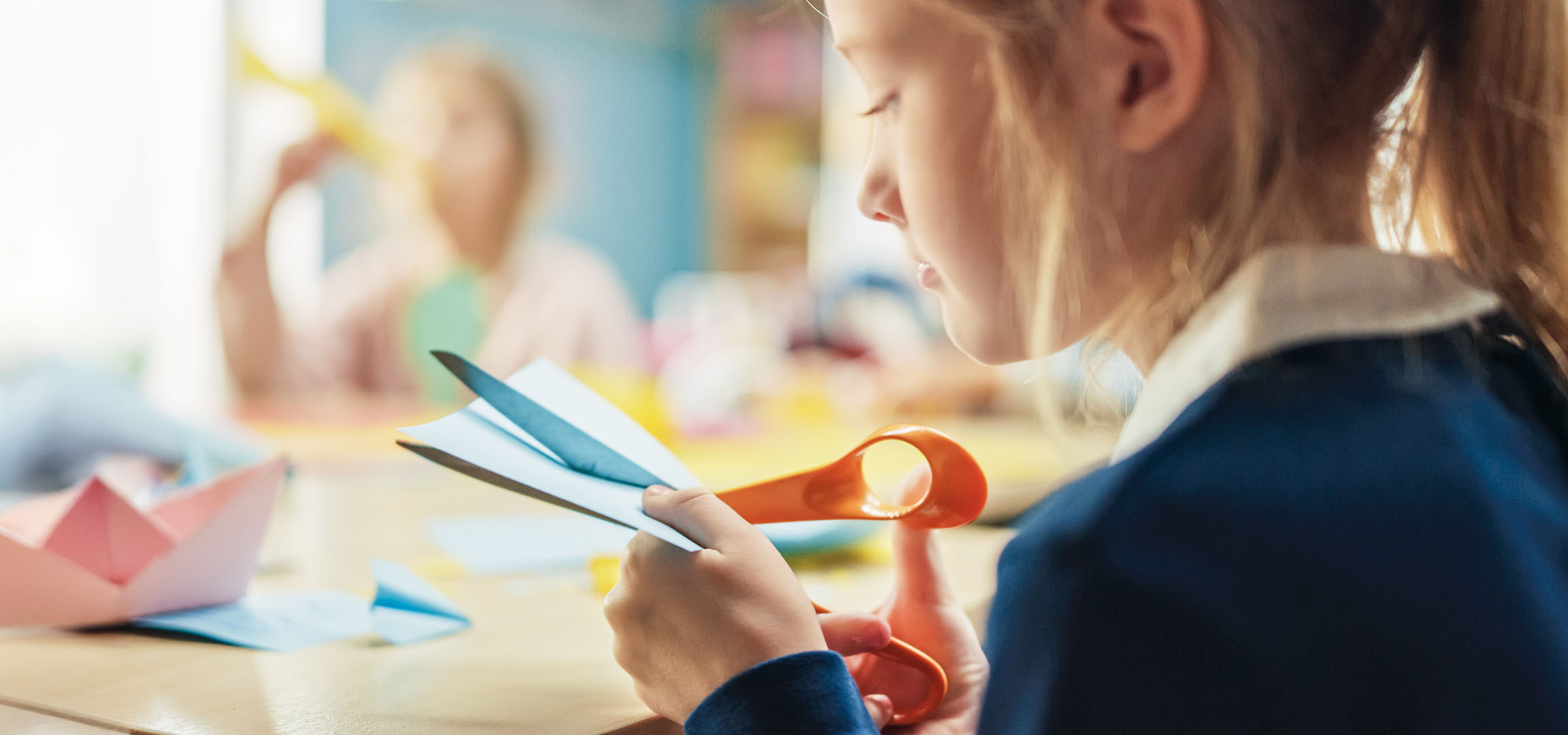 A girl cuts paper to make colorful origami boats.