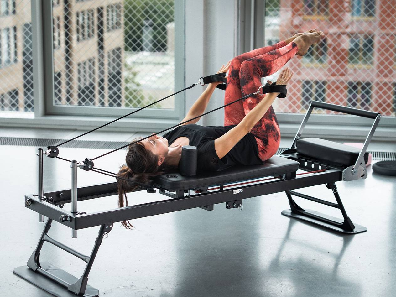Woman exercising Pilates on a reformer with red yoga pants.