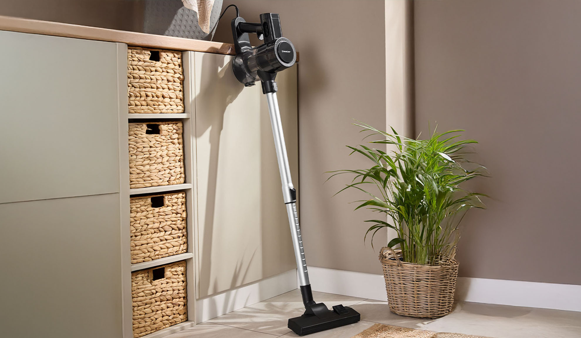 Vacuum cleaner mounted on the wall next to a cabinet with wicker baskets and a plant.