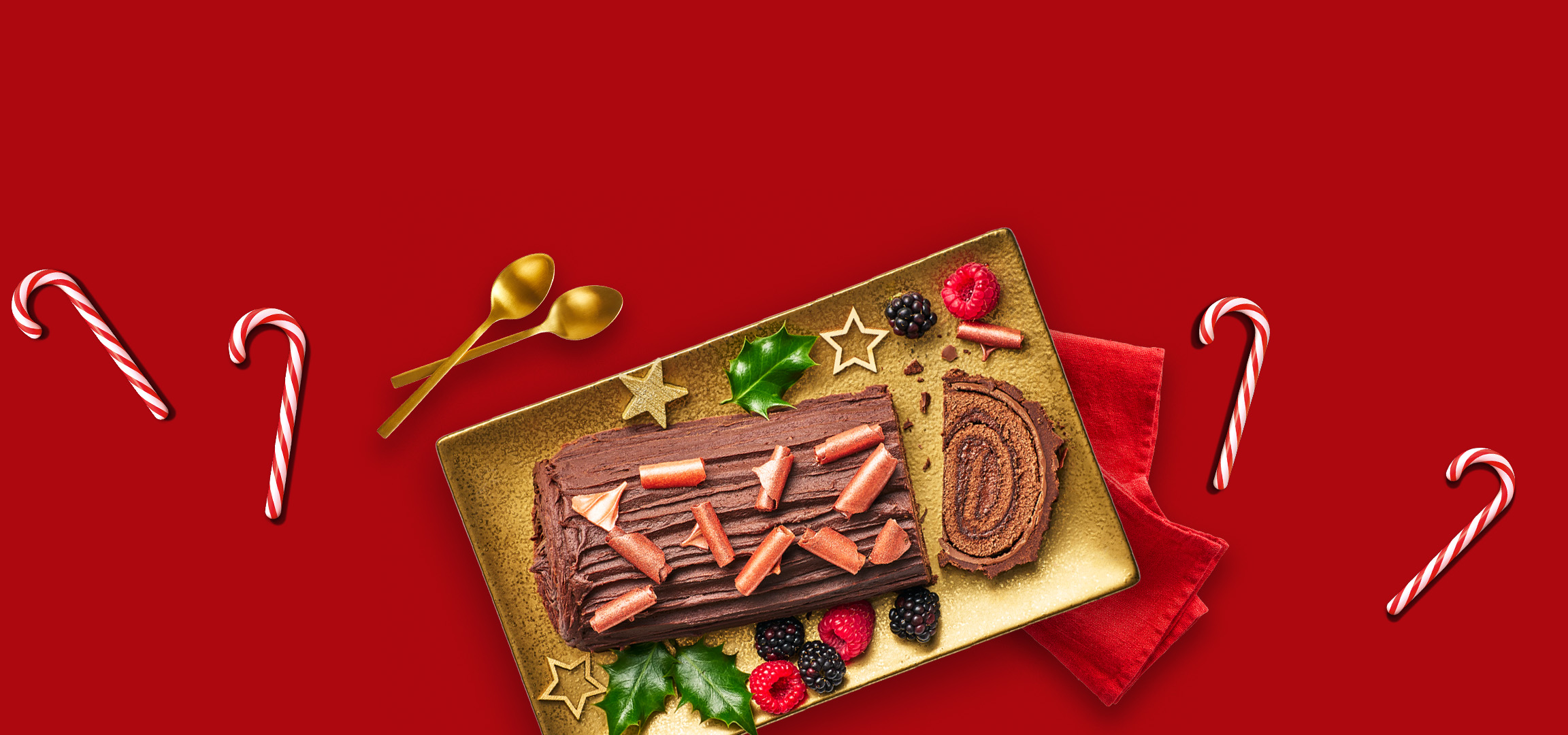 Christmas desserts: chocolate yule log, red berry cheesecake, and candy canes on red.