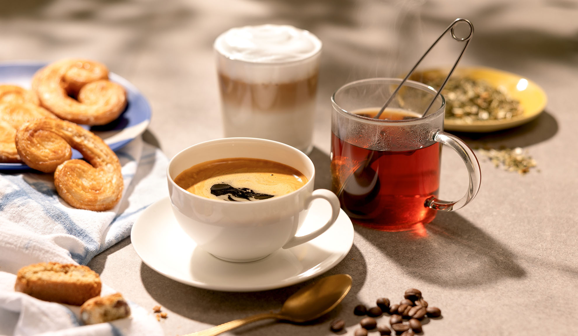 Coffee, tea, and latte with pastries and coffee beans on a table.