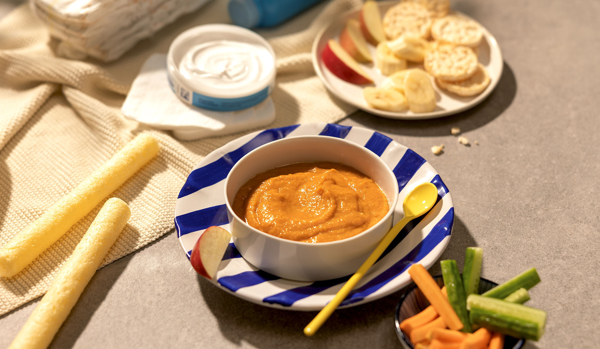 Baby food: bowl of puree, fruit, sticks, and vegetables on a table.