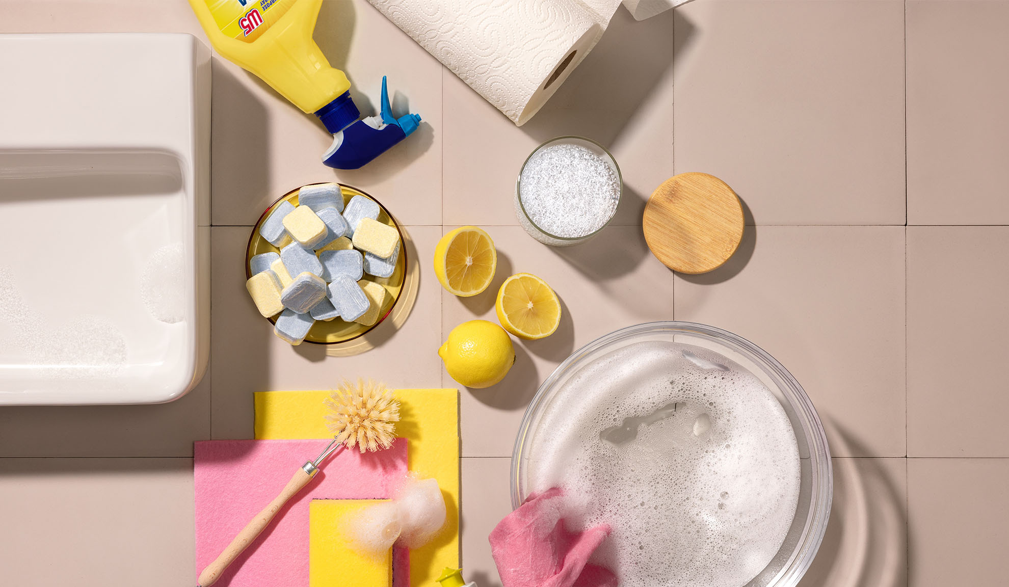 Home cleaning products, including detergent, sponges, lemons, and dishwasher tablets.