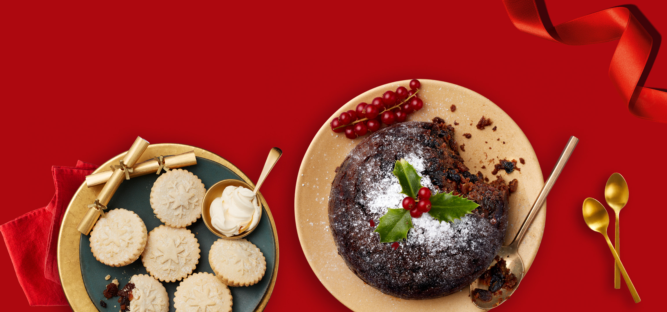 Christmas pudding with redcurrants and holly, mince pies with cream, and golden spoons on red.