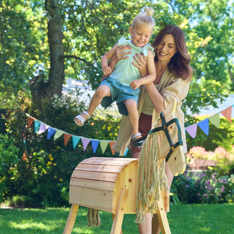 Woman and girl playing with a wooden rocking horse in a garden with bunting.