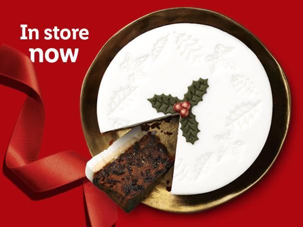 Christmas fruit cake with white icing and holly decoration, with a slice removed.