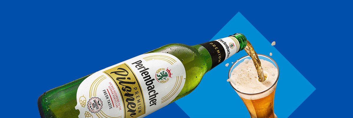A bottle of Perlenbacher Premium Pilsner beer pouring into a glass against a blue background.