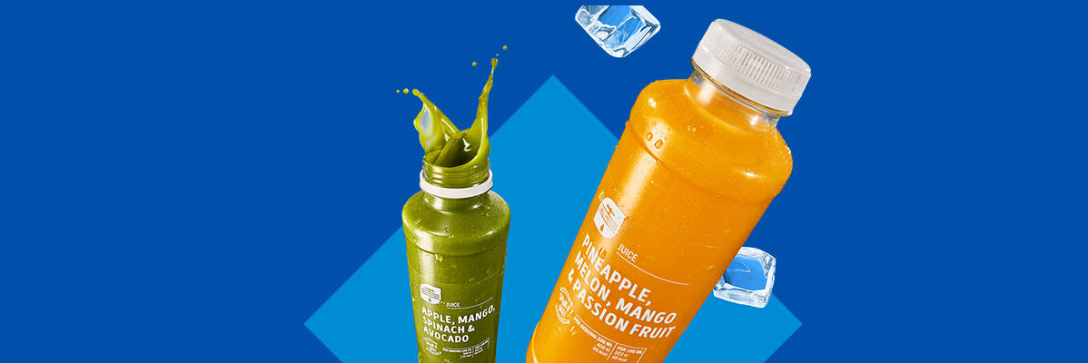 Two juice bottles, one green and one orange, with ice cubes on a blue background.