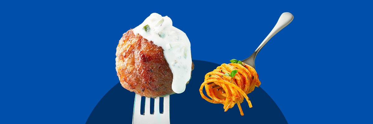 A meatball with white sauce on a fork next to spaghetti on another fork.