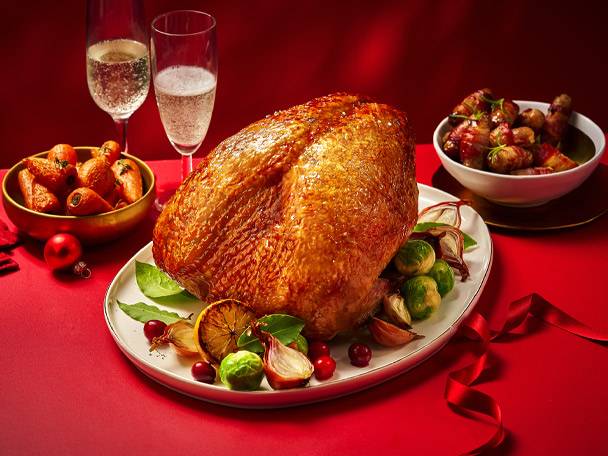 A roasted turkey with sides of vegetables and two glasses of sparkling wine on a red table.
