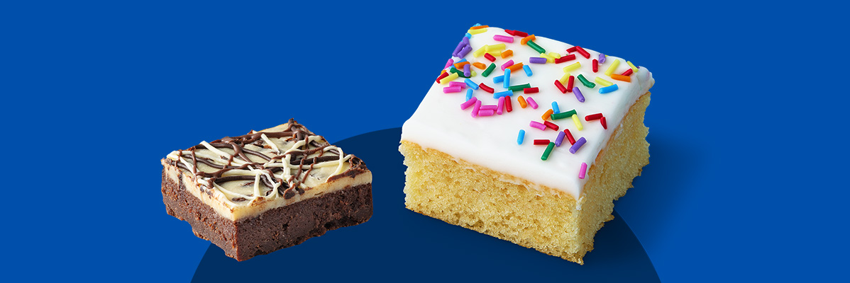 A brownie with white and dark chocolate drizzle next to a vanilla cake with sprinkles.
