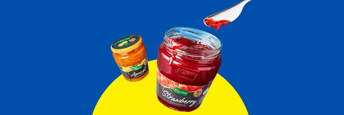 Jars of Maribel apricot and strawberry conserve with a spoon of strawberry jam.
