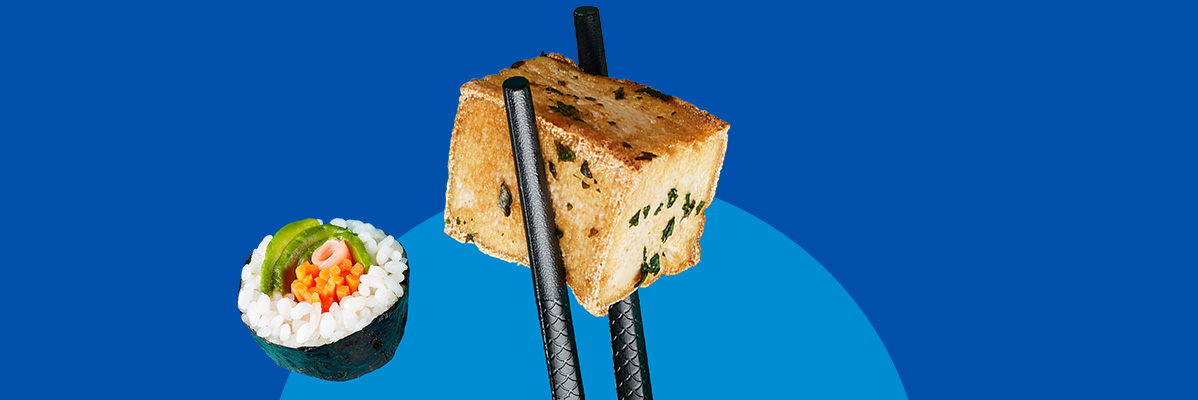 A sushi roll and a block of fried tofu held by chopsticks on a blue background.