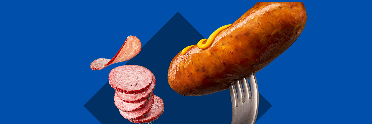 A sausage on a fork with mustard, and a stack of salami slices with one floating.