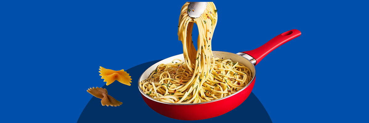 Spaghetti with herbs and chili flakes in a red pan, with two bow-tie pasta pieces.