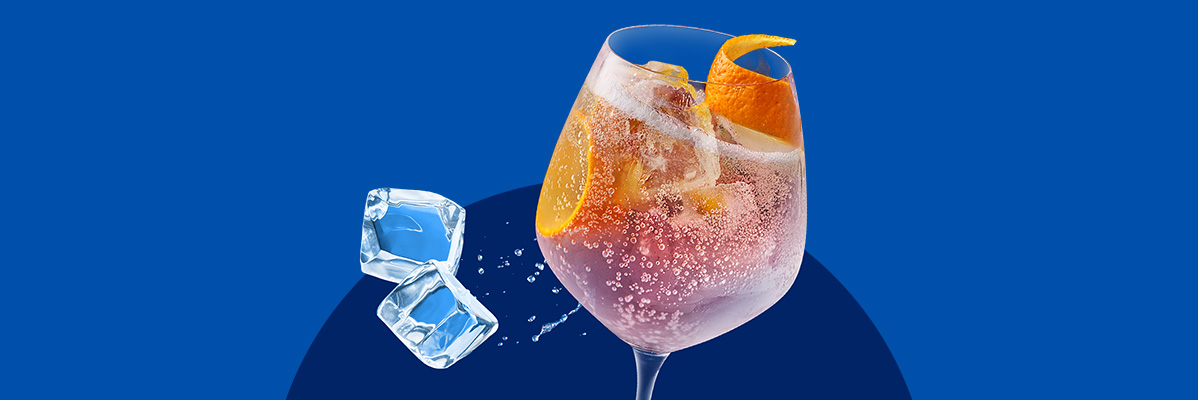 A refreshing pink cocktail with orange slices and ice cubes on a blue background.
