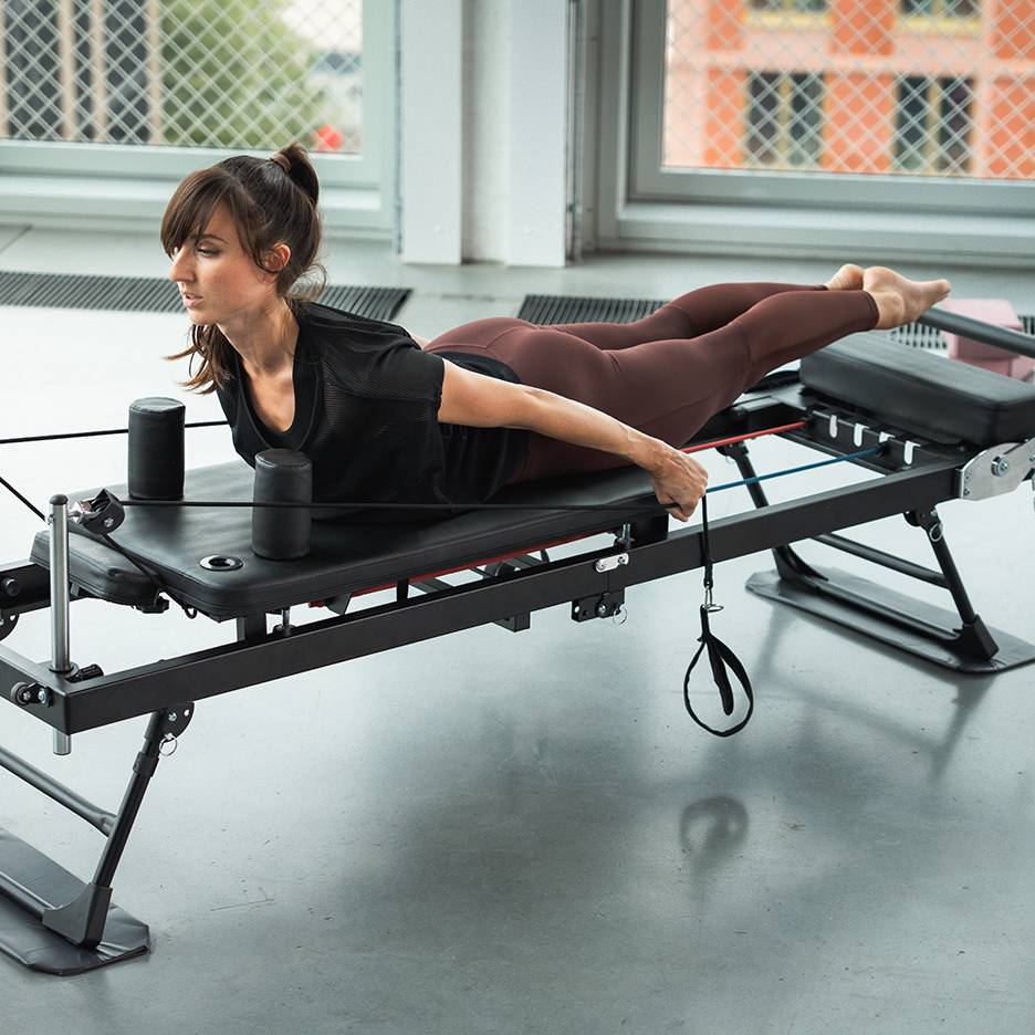 Woman exercising on a Pilates reformer machine with resistance bands.