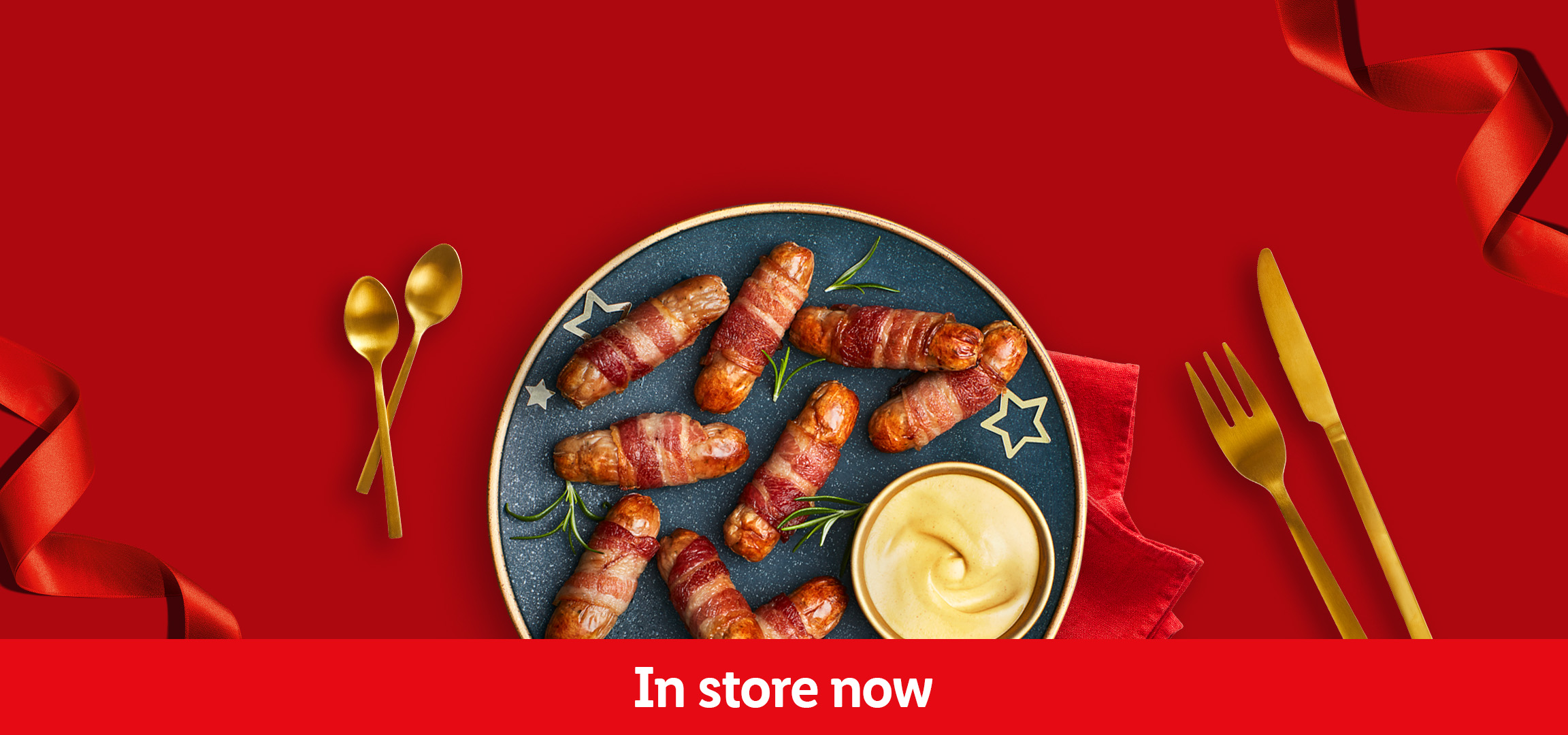 Smoked salmon with lemon and pigs in blankets with mustard on a red background, 'In store now'.