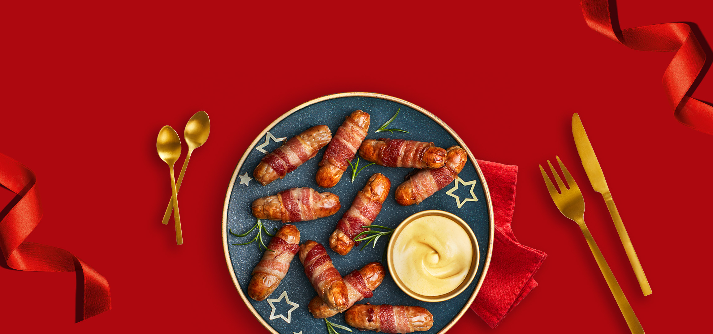 Smoked salmon with lemon and pigs in blankets with mustard on a red background.
