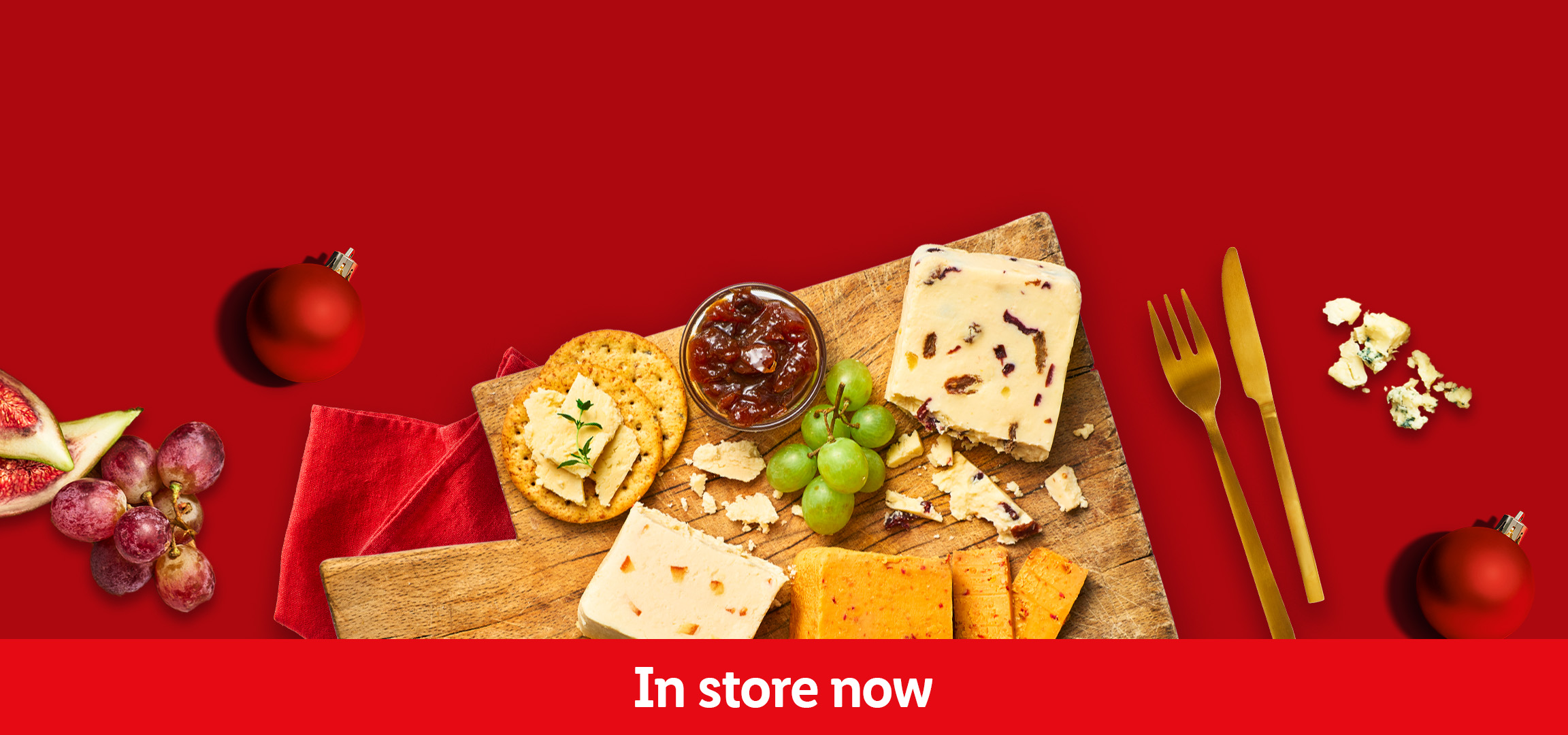 Cheese board with crackers, grapes, figs, chutney, and Christmas decorations. In store now.