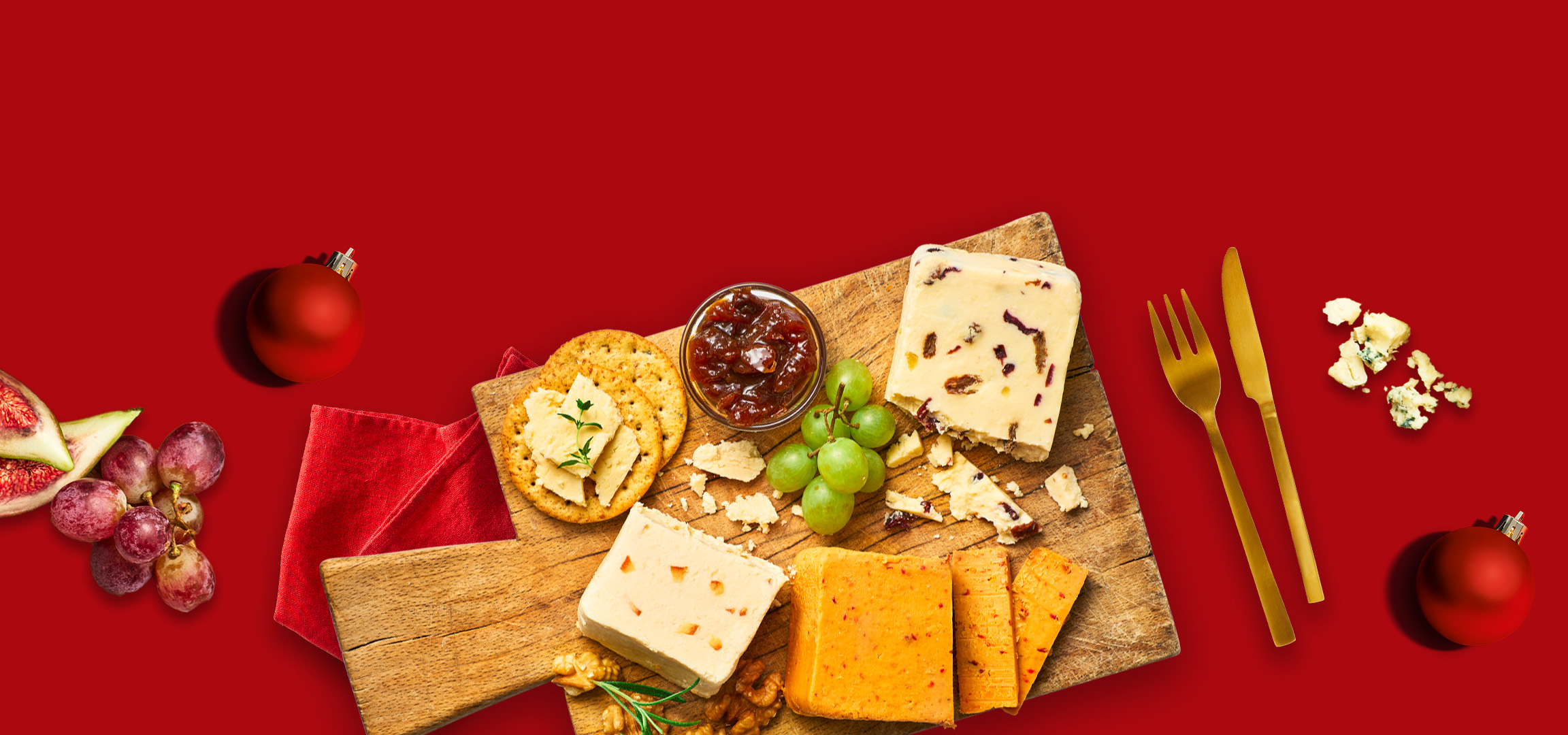 Christmas cheese board with crackers, grapes, figs, and chutney on a red background.