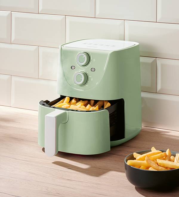 A light green air fryer with a basket of french fries, next to a bowl of fries.