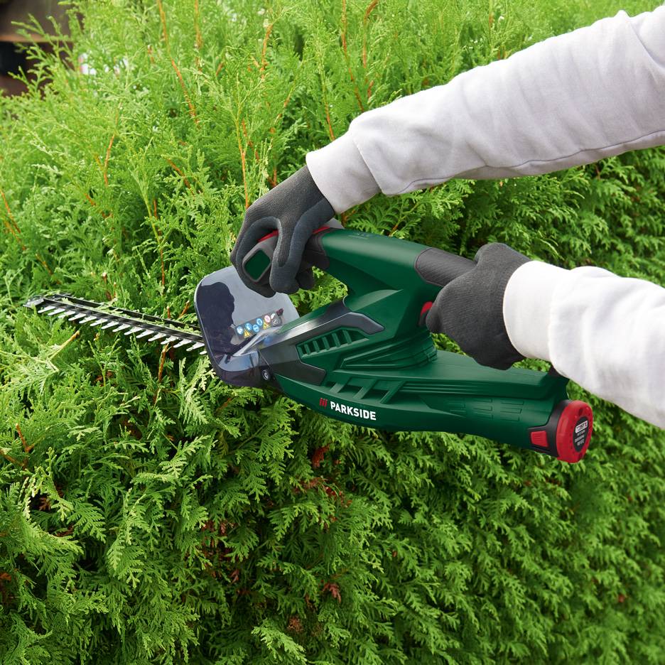 Person trimming a hedge with green Parkside cordless hedge trimmers.
