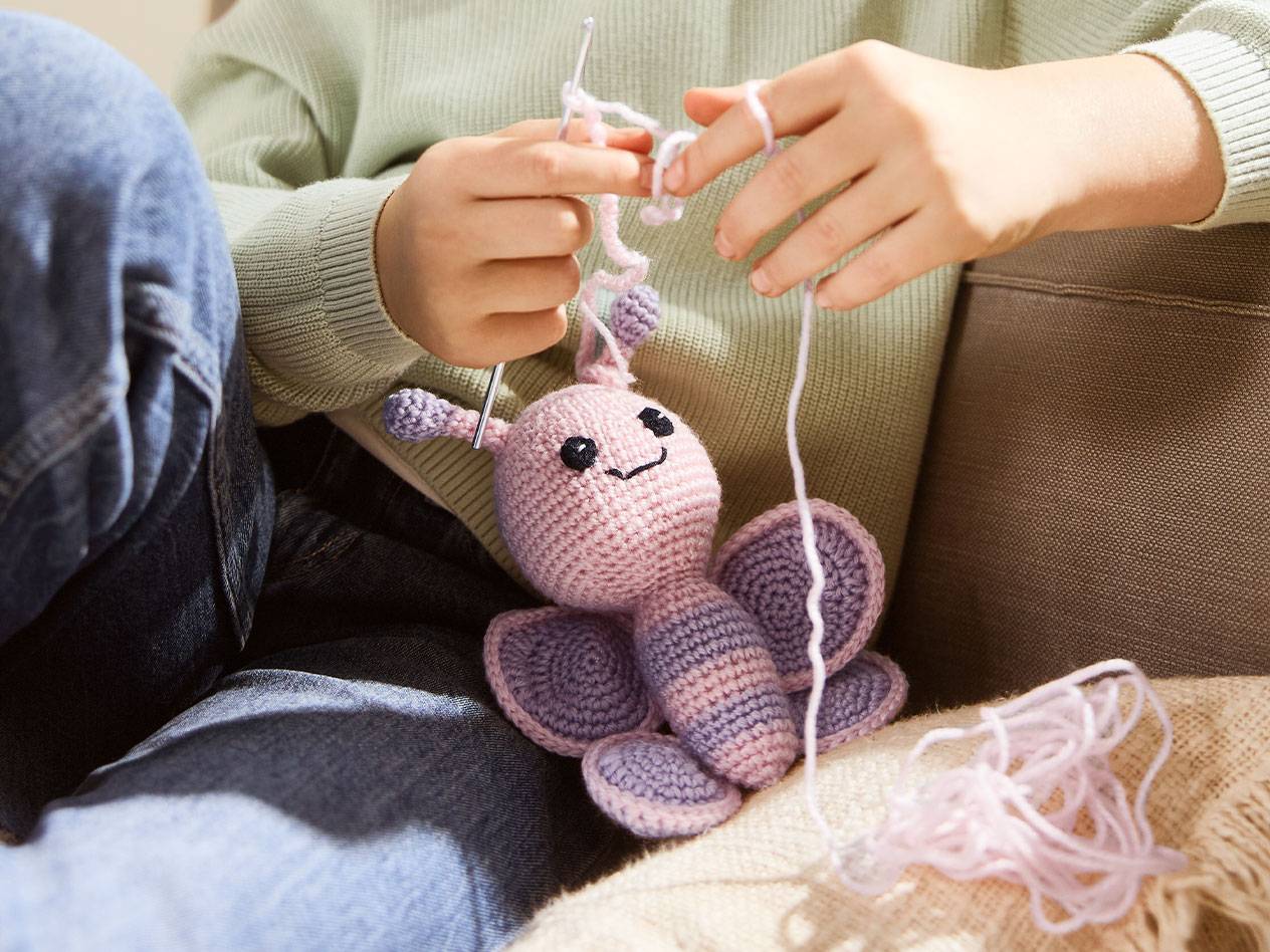 Person crocheting a pink butterfly toy with yarn and a crochet hook.