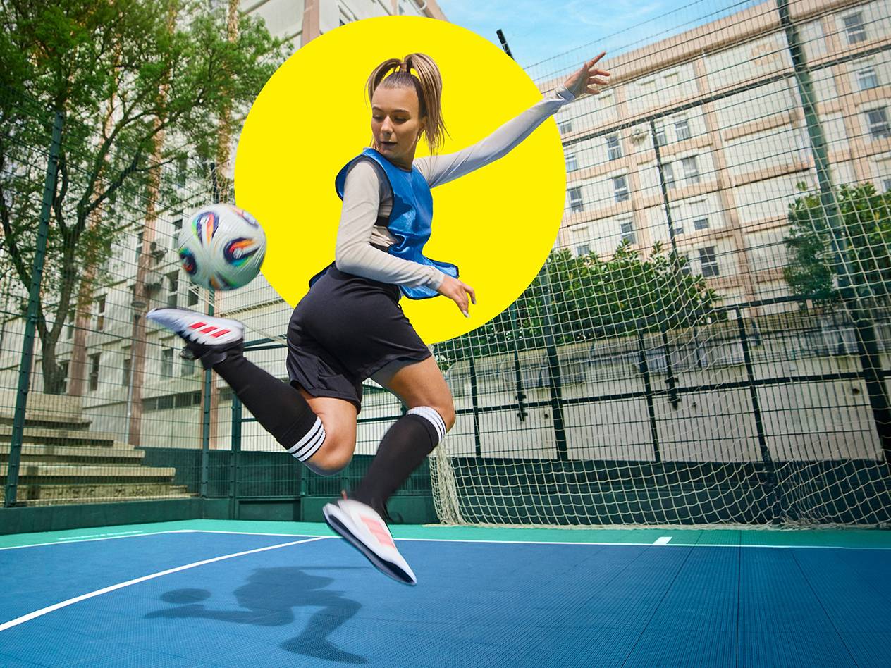 A woman juggles a soccer ball in the air on a soccer field.