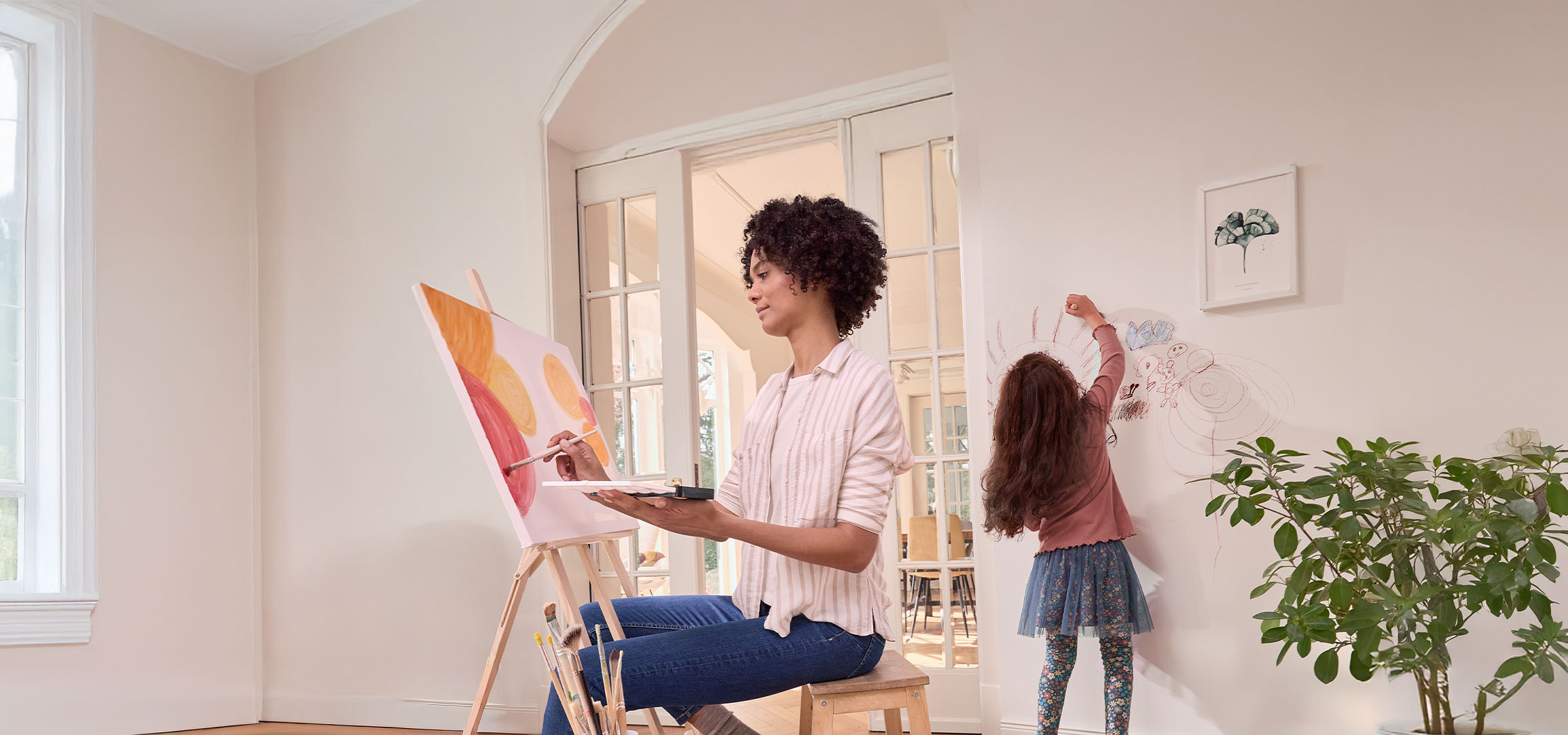 Woman painting on an easel while a child draws on the wall.