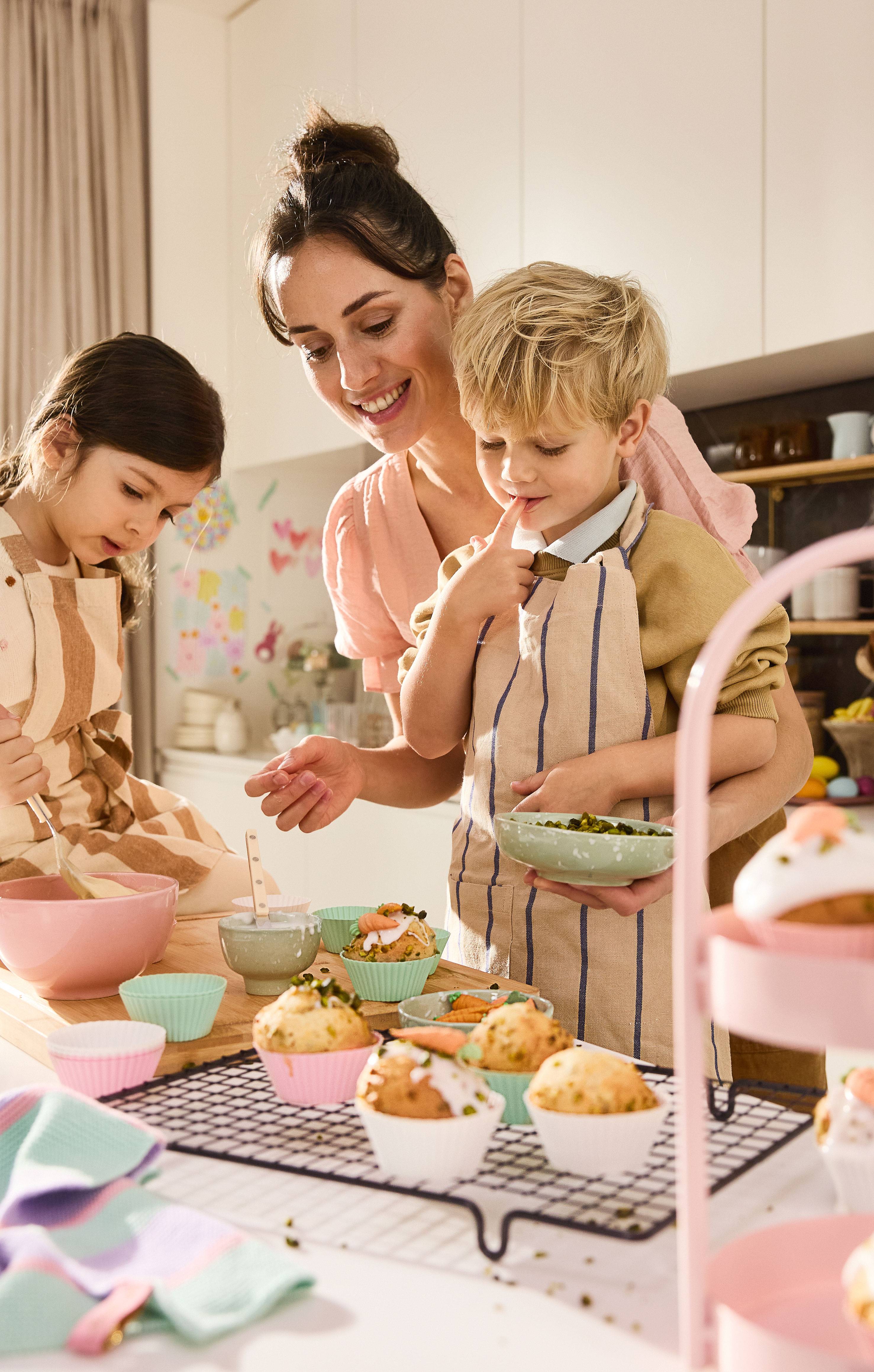 Mother and children decorating Easter muffins with icing and pistachios.