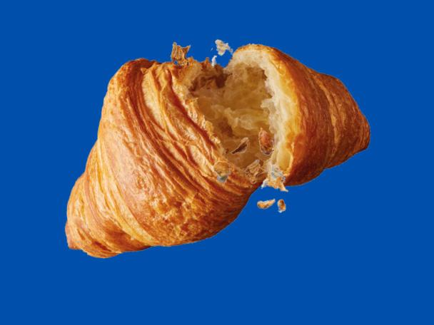 A golden-brown croissant, broken in half with crumbs falling, against a blue background.