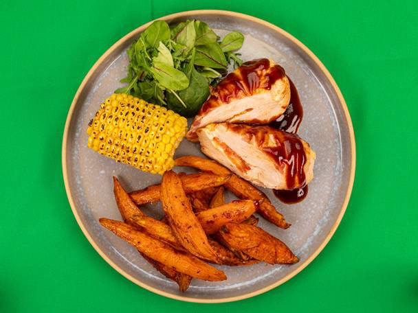 Chicken with sweet potato fries, corn on the cob, and a side salad.