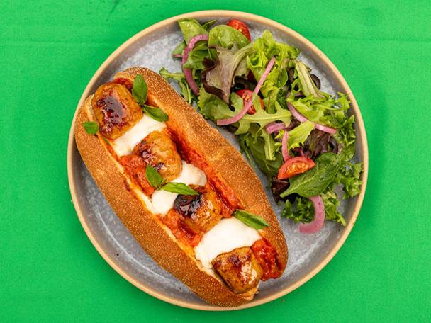 Meatball sub with melted cheese and tomato sauce, served with a side salad.