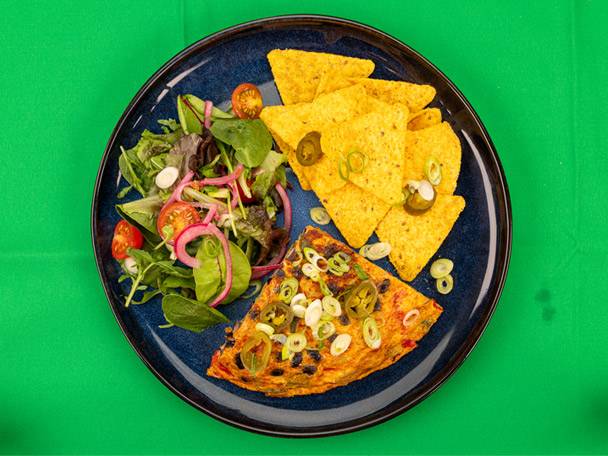 A plate with a slice of frittata, nachos, and a fresh green salad.
