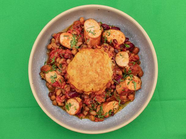 Hearty bean stew with sausages and a golden-brown dumpling, garnished with fresh herbs.