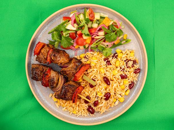 Grilled meat skewers with rice and beans, and a side salad on a plate.