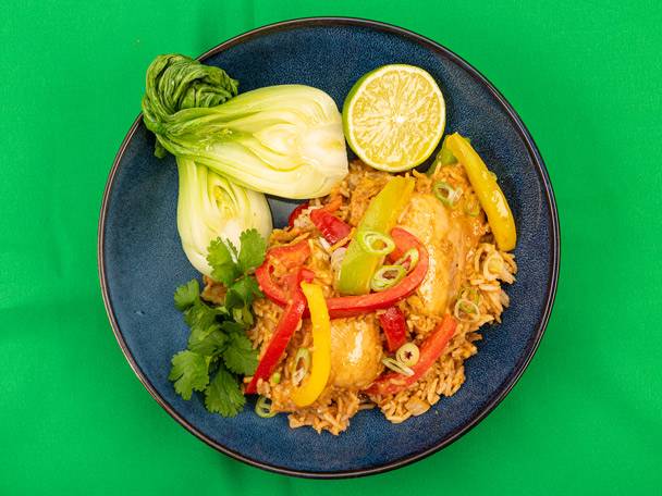 Chicken curry with rice, bell peppers, bok choy, and lime on a blue plate.