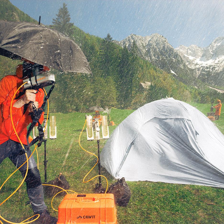 Person in rain gear testing camping equipment in the rain with mountains in the background.