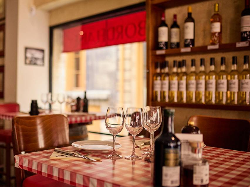 Restaurant table with red and white checkered tablecloth, wine glasses, and wine bottles.
